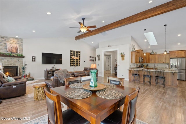 dining space featuring a fireplace, recessed lighting, lofted ceiling with skylight, a ceiling fan, and light wood-type flooring