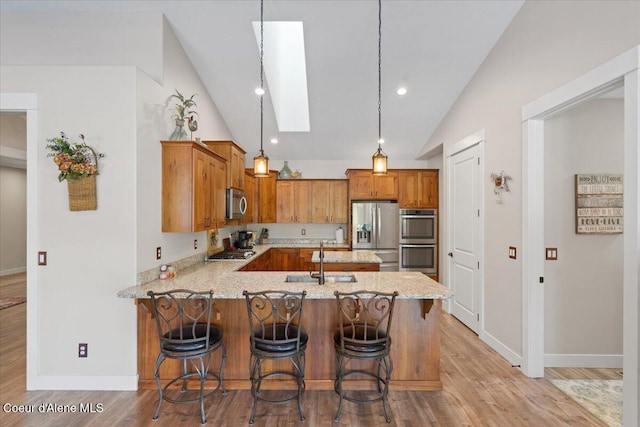 kitchen featuring light stone countertops, stainless steel appliances, a peninsula, a sink, and brown cabinets