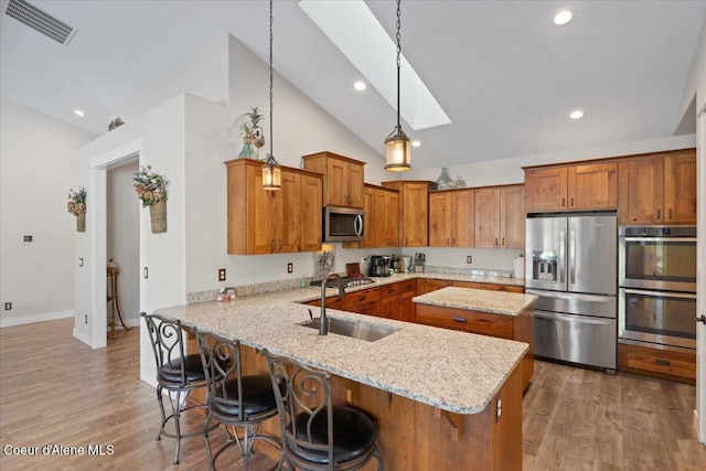 kitchen featuring a skylight, brown cabinets, stainless steel appliances, visible vents, and a sink