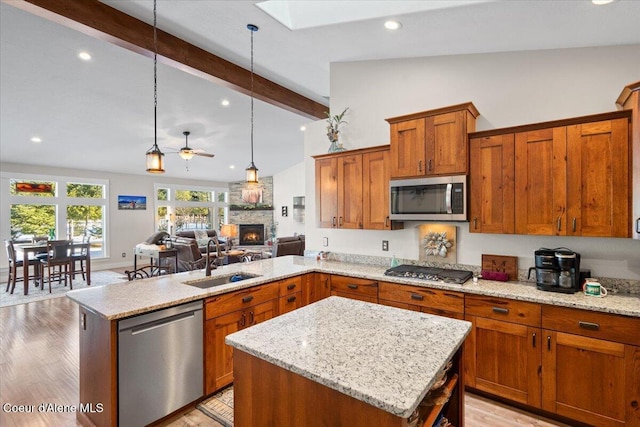 kitchen featuring lofted ceiling with skylight, appliances with stainless steel finishes, a peninsula, a fireplace, and a sink