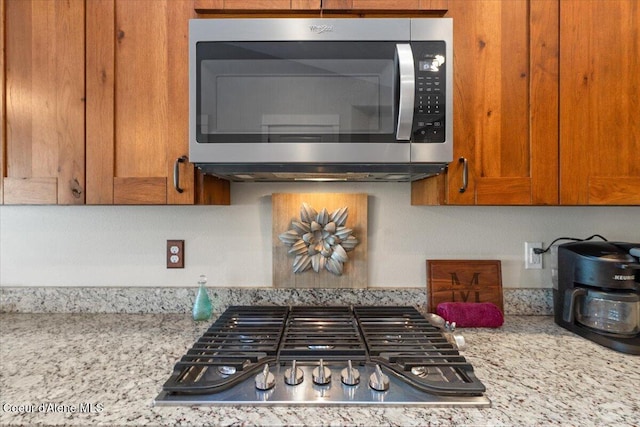 details with appliances with stainless steel finishes, brown cabinets, and light stone counters