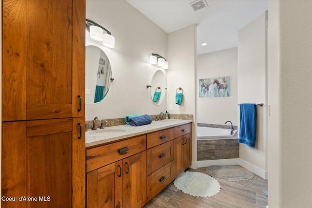 bathroom featuring visible vents, a sink, a bath, and wood finished floors