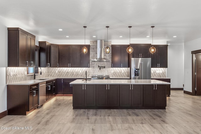 kitchen featuring pendant lighting, appliances with stainless steel finishes, a kitchen island, wall chimney range hood, and sink