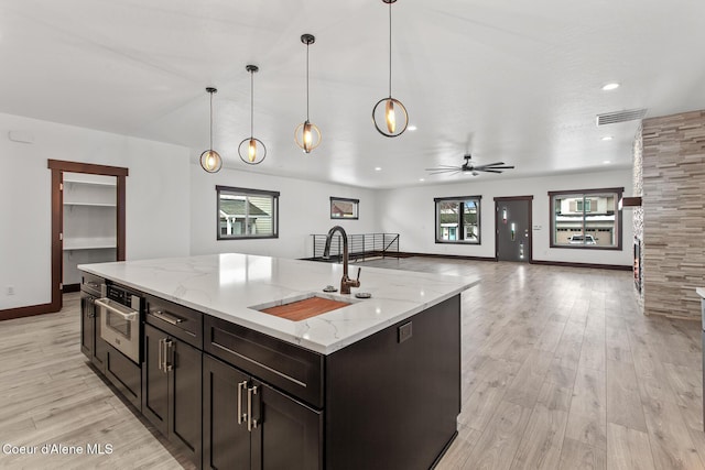 kitchen with ceiling fan, a center island with sink, pendant lighting, sink, and light stone counters