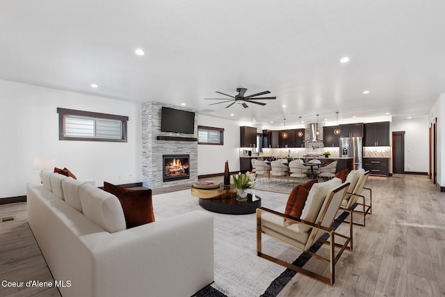 living room with ceiling fan, light wood-type flooring, and a large fireplace