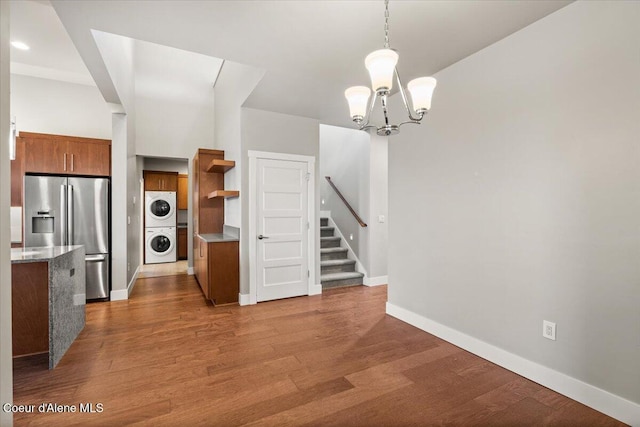 kitchen with pendant lighting, dark hardwood / wood-style flooring, an inviting chandelier, stainless steel fridge, and stacked washer and clothes dryer