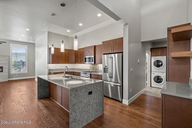 kitchen with a center island with sink, pendant lighting, sink, stacked washer and clothes dryer, and stainless steel appliances