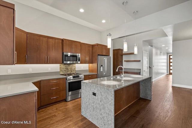 kitchen with decorative light fixtures, dark hardwood / wood-style floors, sink, a kitchen island with sink, and stainless steel appliances