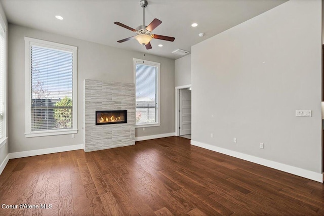 unfurnished living room featuring ceiling fan, a tiled fireplace, and dark wood-type flooring