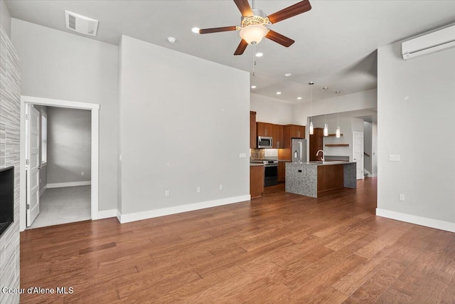 unfurnished living room with an AC wall unit, sink, ceiling fan, and dark wood-type flooring