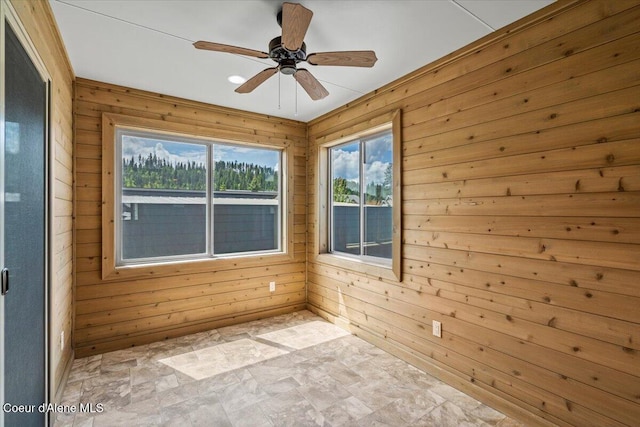 spare room with ceiling fan, wood walls, and a healthy amount of sunlight