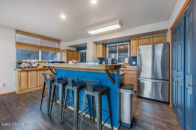 kitchen with a kitchen island, stainless steel refrigerator, a breakfast bar area, and dark wood-type flooring