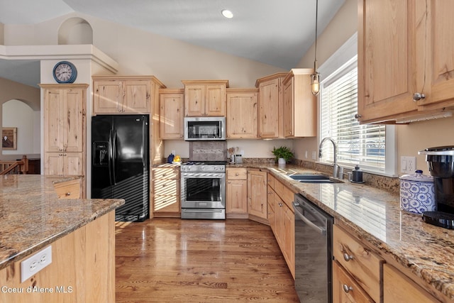 kitchen with appliances with stainless steel finishes, sink, hanging light fixtures, light stone counters, and light hardwood / wood-style flooring