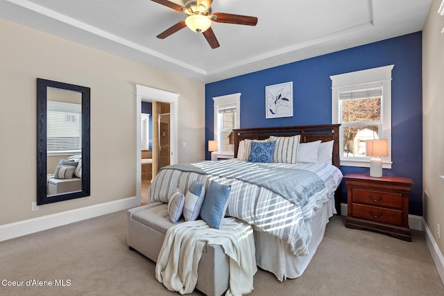 bedroom featuring a raised ceiling, ceiling fan, light carpet, and ensuite bathroom