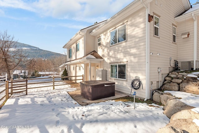 snow covered house featuring a mountain view, cooling unit, and a hot tub