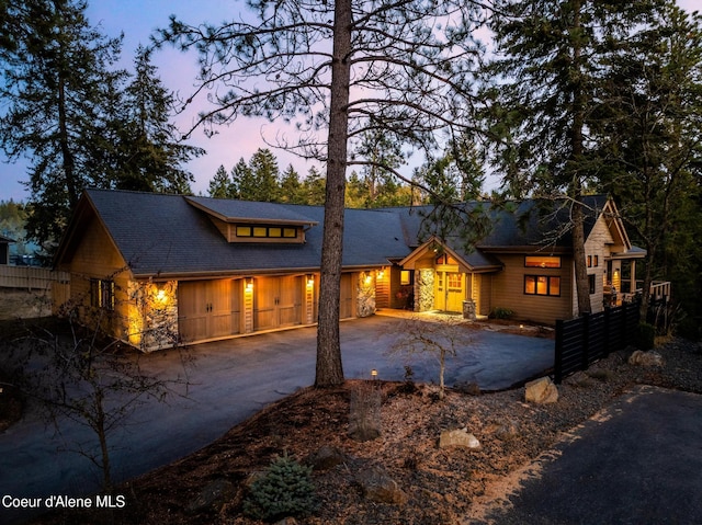 view of front facade featuring stone siding, fence, and aphalt driveway