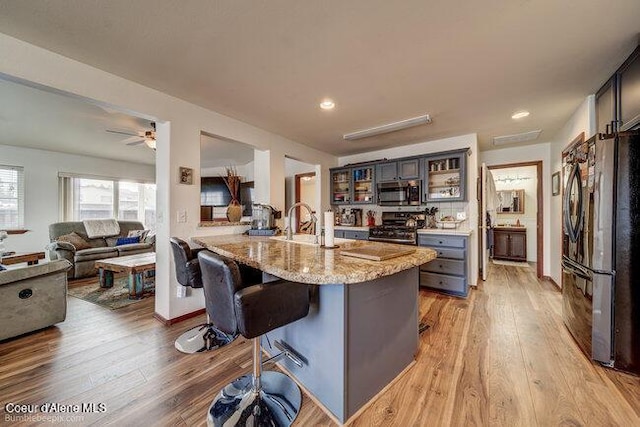 kitchen featuring a kitchen bar, stainless steel appliances, light hardwood / wood-style floors, light stone counters, and a center island with sink