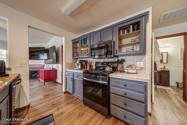 kitchen with light wood-type flooring, backsplash, gray cabinetry, and stainless steel appliances