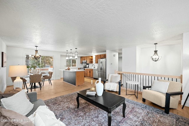 living room with a textured ceiling, a chandelier, light hardwood / wood-style floors, and sink