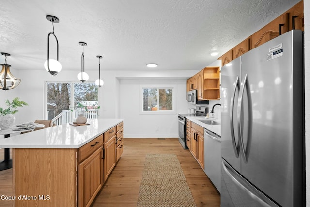 kitchen with decorative light fixtures, light wood-type flooring, stainless steel appliances, and a textured ceiling