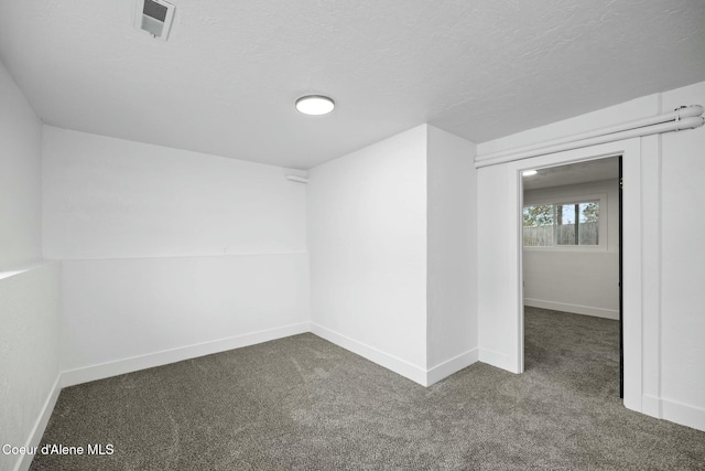 spare room featuring dark carpet and a textured ceiling