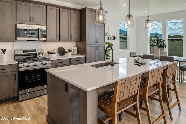 kitchen with a center island with sink, sink, dark brown cabinetry, hanging light fixtures, and stainless steel appliances