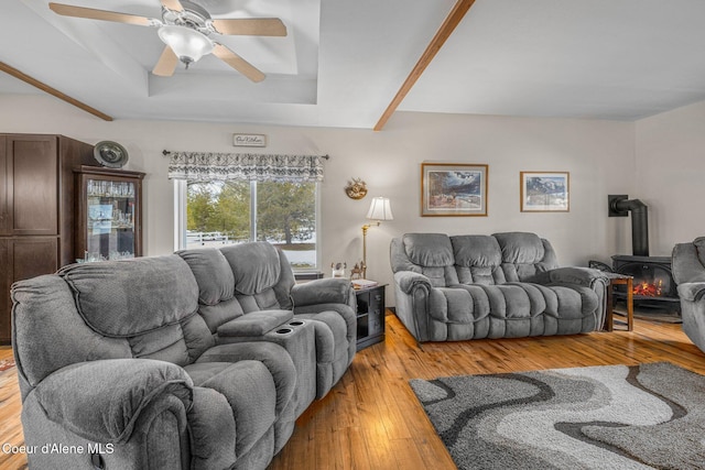 living room featuring ceiling fan, a tray ceiling, a wood stove, and light wood-type flooring