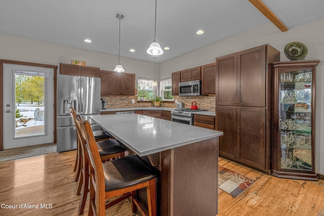 kitchen with appliances with stainless steel finishes, pendant lighting, backsplash, a center island, and beam ceiling