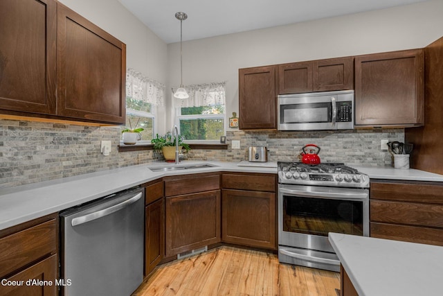 kitchen with pendant lighting, sink, appliances with stainless steel finishes, tasteful backsplash, and light hardwood / wood-style floors