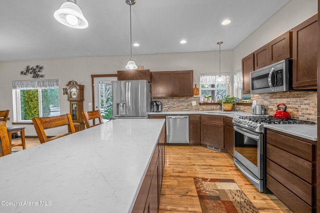 kitchen with sink, appliances with stainless steel finishes, hanging light fixtures, light hardwood / wood-style floors, and decorative backsplash