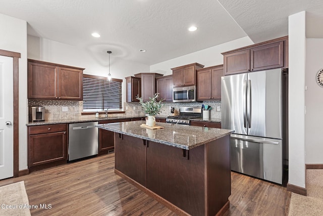 kitchen with a kitchen island, dark hardwood / wood-style flooring, hanging light fixtures, stainless steel appliances, and dark stone counters