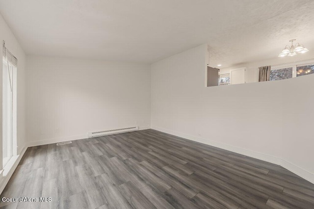 empty room featuring baseboard heating, hardwood / wood-style floors, and a notable chandelier