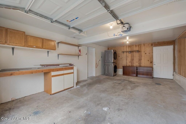 garage with wooden walls, a garage door opener, and stacked washing maching and dryer