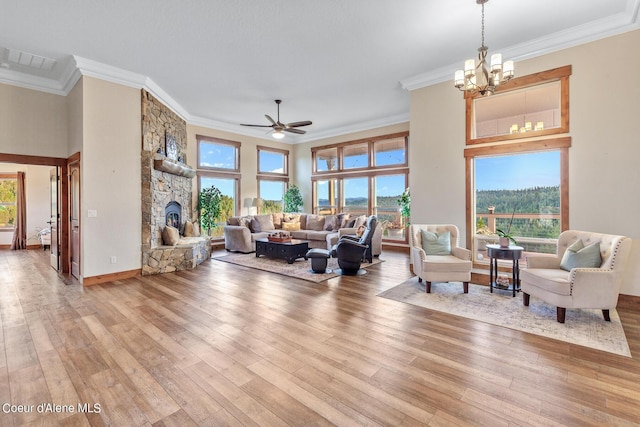 living room with light hardwood / wood-style floors, ornamental molding, a stone fireplace, and ceiling fan with notable chandelier