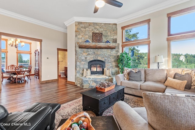 living room featuring crown molding, ceiling fan with notable chandelier, wood-type flooring, and a stone fireplace