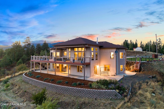 back house at dusk featuring a deck and a patio