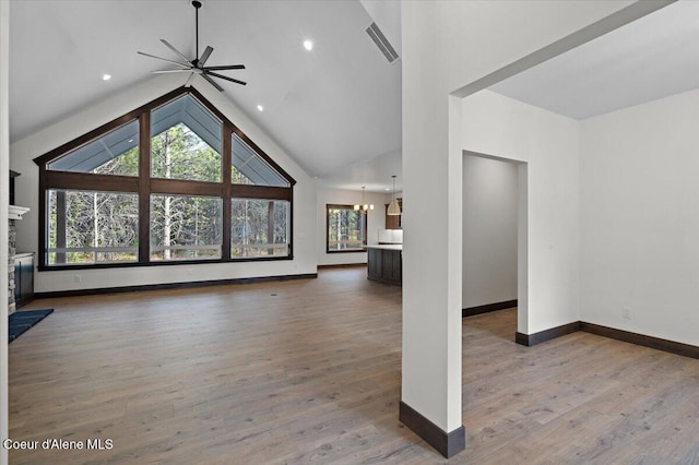 unfurnished living room with lofted ceiling, ceiling fan with notable chandelier, and wood-type flooring