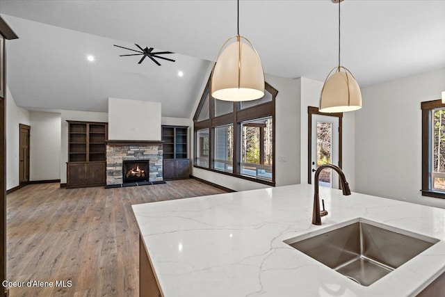 kitchen featuring pendant lighting, a stone fireplace, sink, vaulted ceiling, and light stone counters