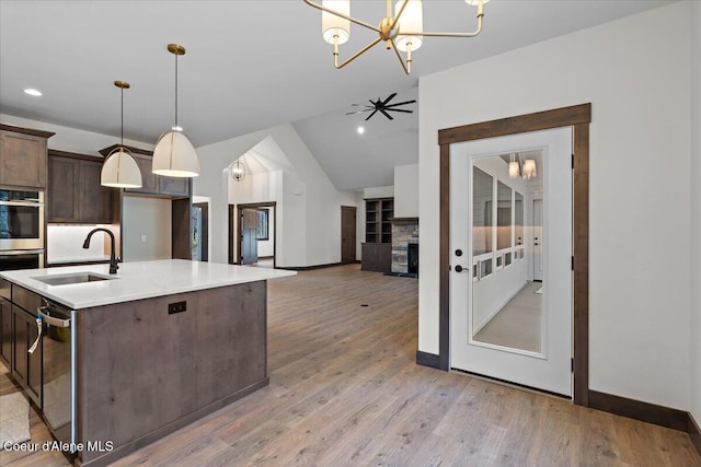 kitchen featuring sink, hanging light fixtures, a stone fireplace, dark brown cabinets, and ceiling fan with notable chandelier