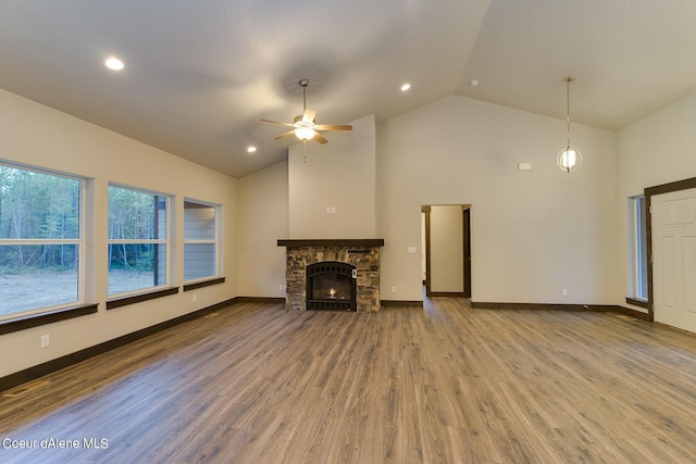 unfurnished living room with high vaulted ceiling, ceiling fan, wood-type flooring, and a stone fireplace