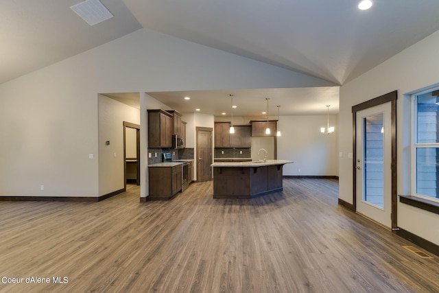 kitchen with pendant lighting, stainless steel appliances, decorative backsplash, a kitchen island with sink, and vaulted ceiling