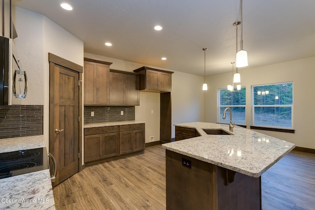 kitchen with hardwood / wood-style floors, decorative backsplash, sink, hanging light fixtures, and light stone countertops