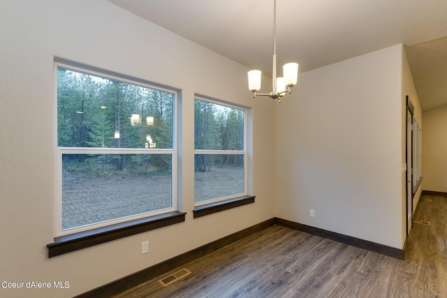 unfurnished dining area with a wealth of natural light, dark hardwood / wood-style flooring, and a notable chandelier