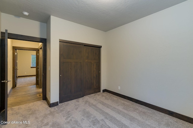 unfurnished bedroom featuring a textured ceiling, a closet, and light carpet