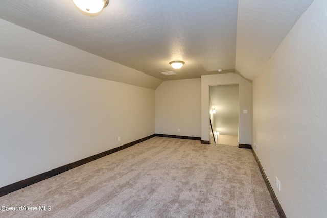 additional living space featuring vaulted ceiling, a textured ceiling, and light colored carpet