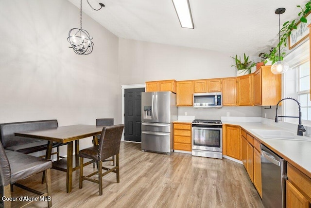 kitchen with sink, decorative light fixtures, high vaulted ceiling, light hardwood / wood-style flooring, and stainless steel appliances