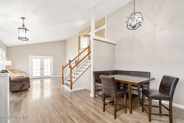 dining space with lofted ceiling, an inviting chandelier, light wood-type flooring, and french doors