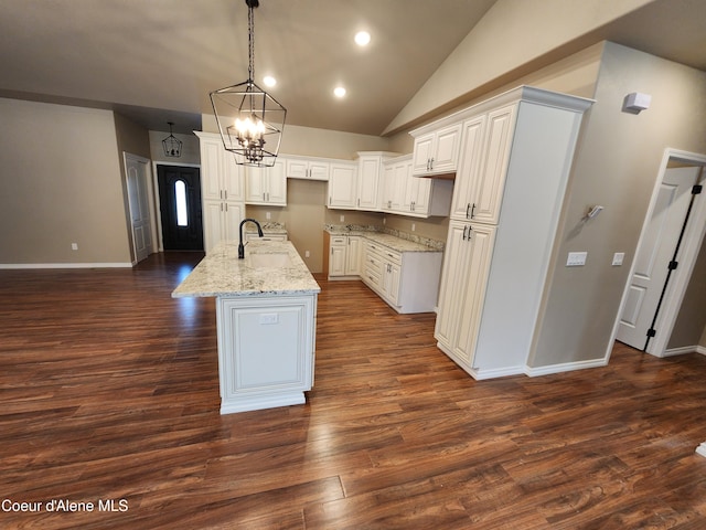 kitchen featuring dark hardwood / wood-style floors, a center island with sink, pendant lighting, white cabinetry, and light stone counters