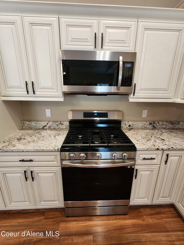 kitchen with appliances with stainless steel finishes, dark hardwood / wood-style flooring, light stone counters, and white cabinetry