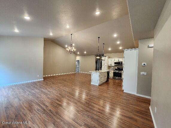 unfurnished living room featuring vaulted ceiling, dark hardwood / wood-style floors, and a notable chandelier